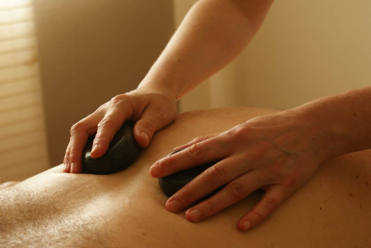 Hotstone Massage Zwei hände massieren mit heißen Steinen Rücken 