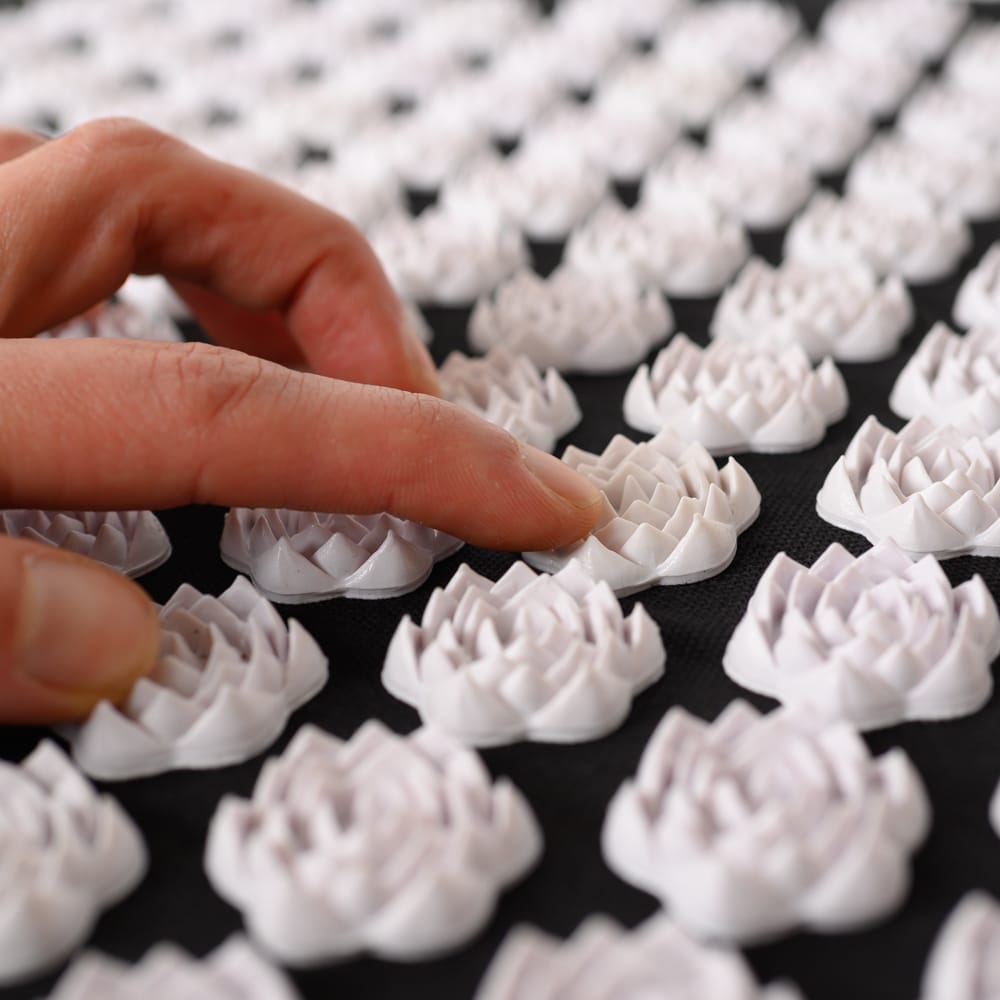 Finger streichen über Spiru Nagelmatte Schwarz Nagelmatte mit weißen Blumen Spitzen auf weißem Hintergrund