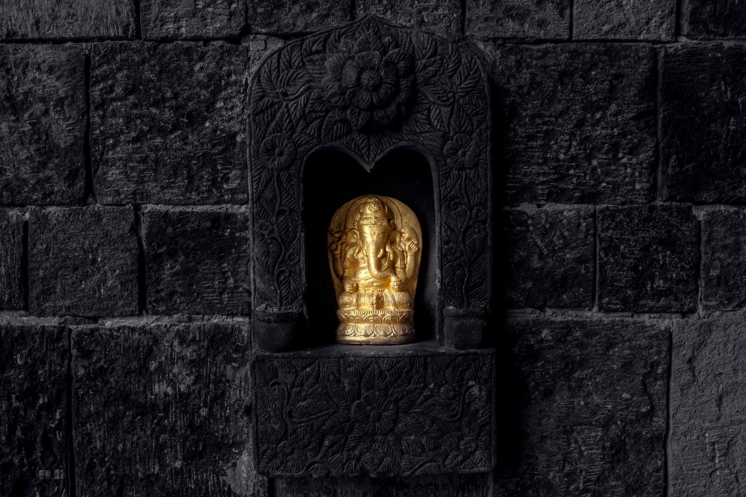 Ganesha Elefantengott Figur Statue Gold auf schwarzen Steinaltar vor schwarzer Mauer
