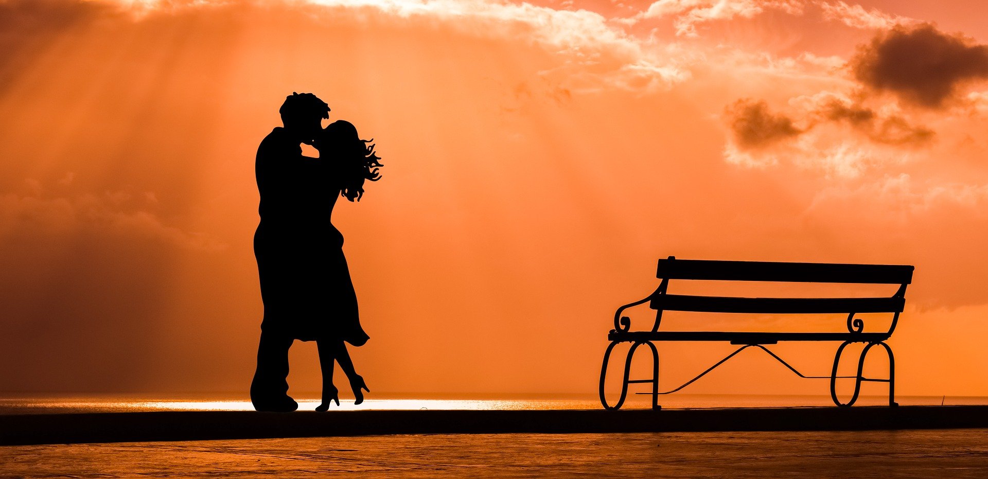 Silhouette Paar küssend mit Bank am meer vor orangenem Sonnenuntergang