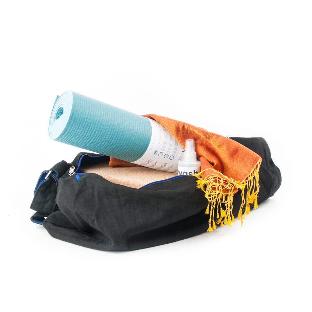 Aufgerollte Yogamatte mit Yogareiniger und Yogablock in schwarzer Tragetasche und orangem Tuch auf weißem Hintergrund