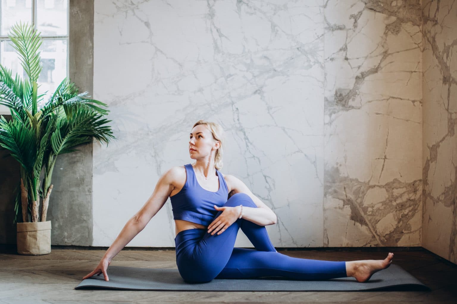 Frau in lila sportkleidung in Yogaposition vor Marmorwand