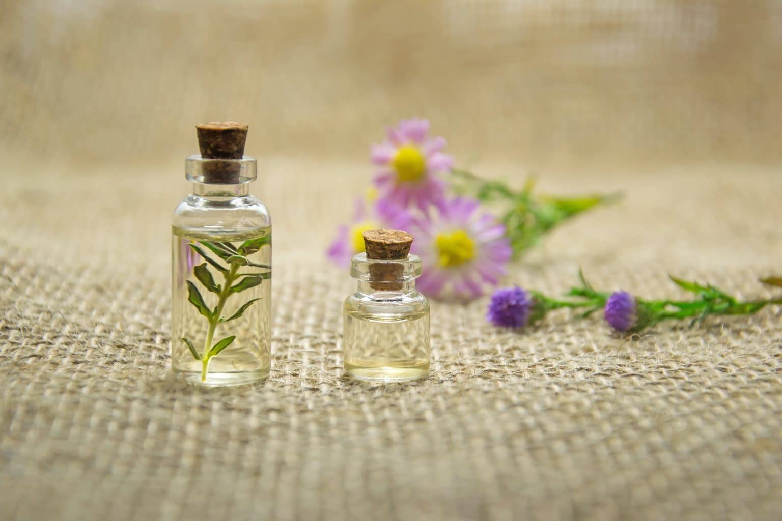 Ätherisches Öl in kleiner Flasche mit Korken und Blumen auf Jute