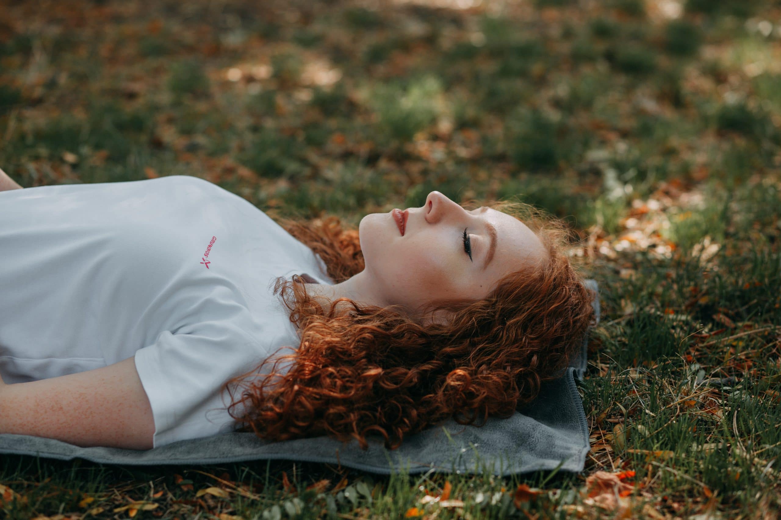 Frau mit roten Haaren und geschlossenen Augen liegend im Gras