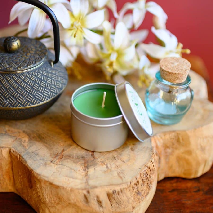 Chakra Kerze Grün mit teepott und Glasfläschchen auf Holz mit weißen Blumen
